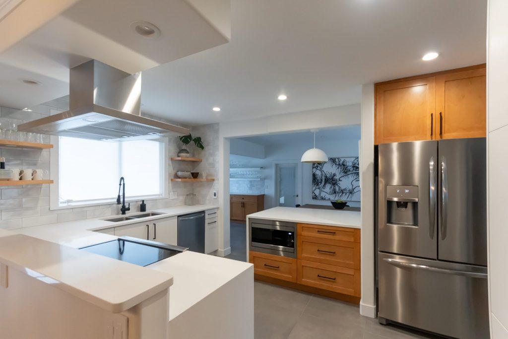 White and wood-grain kitchen with a stainless island hood over the cooktop peninsula and a stainless fridge, Queens Park kitchen renovation in New Westminster